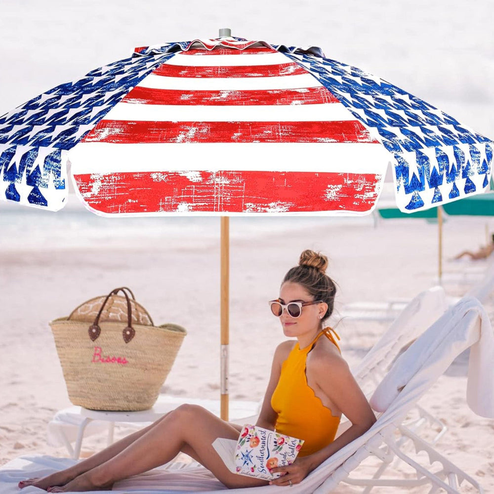 A woman sits on the sandy beach, shaded by an AMMSUN 7.5ft blue red umbrellas for sun protection