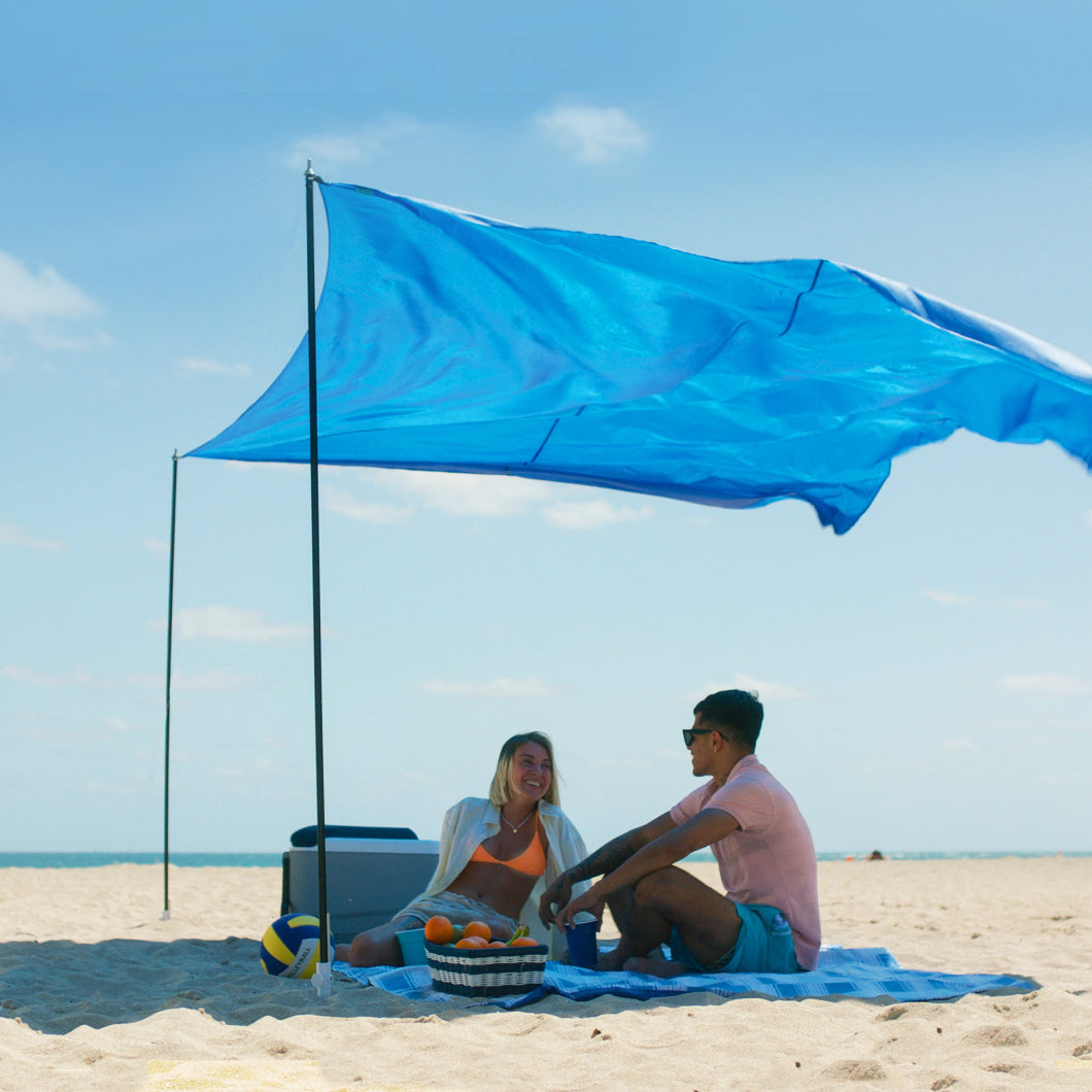 Two peple are sitting under AMMSUN light blue Portable Lycra Beach Tent on the beach providing 9.7×10.1 Sq. Ft shade area