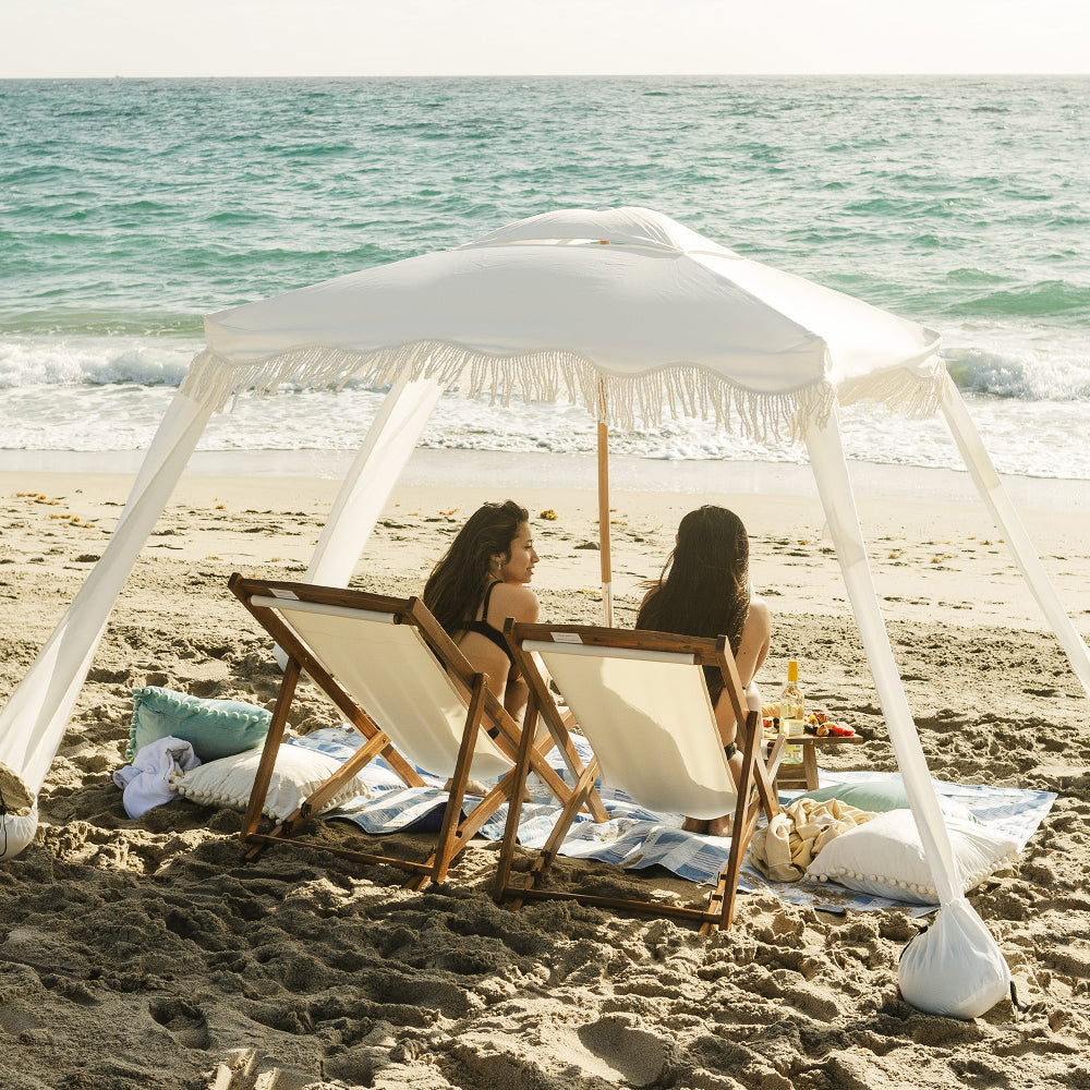 women sitting under AMMSUN 6'×6' Elegant white Bobo Beach Cabana with Fringe on the beach