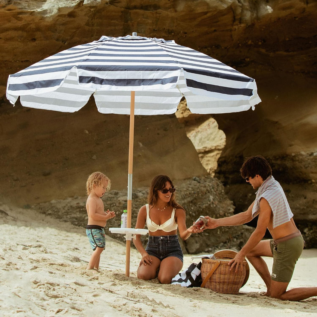 Two people sit with a child under AMMSUN 7.5ft commercial grade navy stripes large beach umbrella on beach