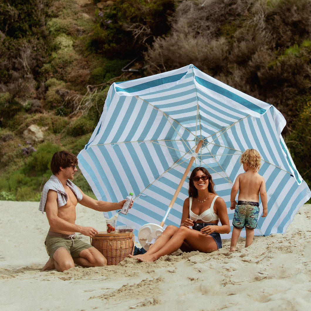 A family of three relaxing under AMMSUN 7.5ft stripe teal white wind resistant beach umbrella