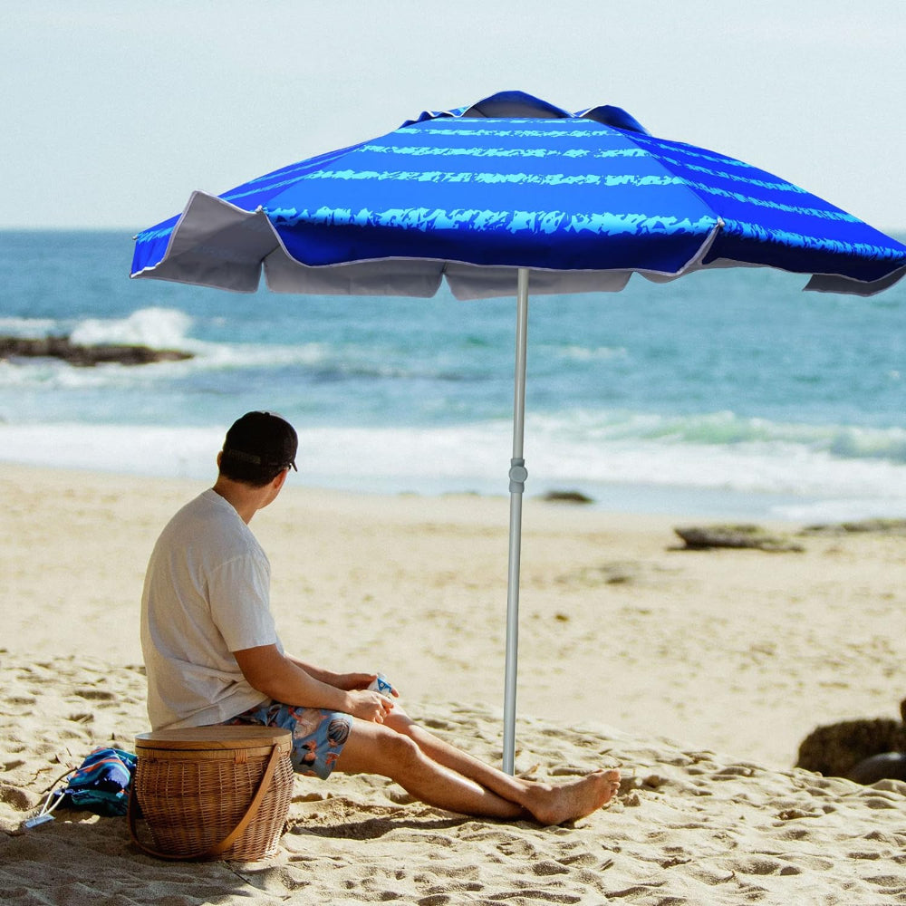 A man relaxes on the beach, seated under a silence blue AMMSUN 6.5ft beach umbrella with anchor