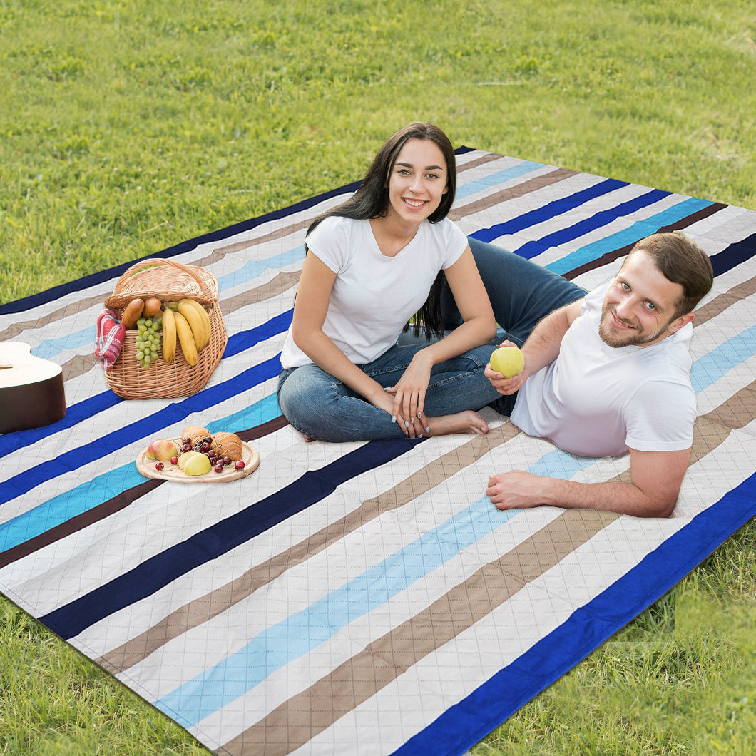 Two people are sitting on AMMSUN Chathams Blue Stripe Beach Blanket, Extra Large 94.5