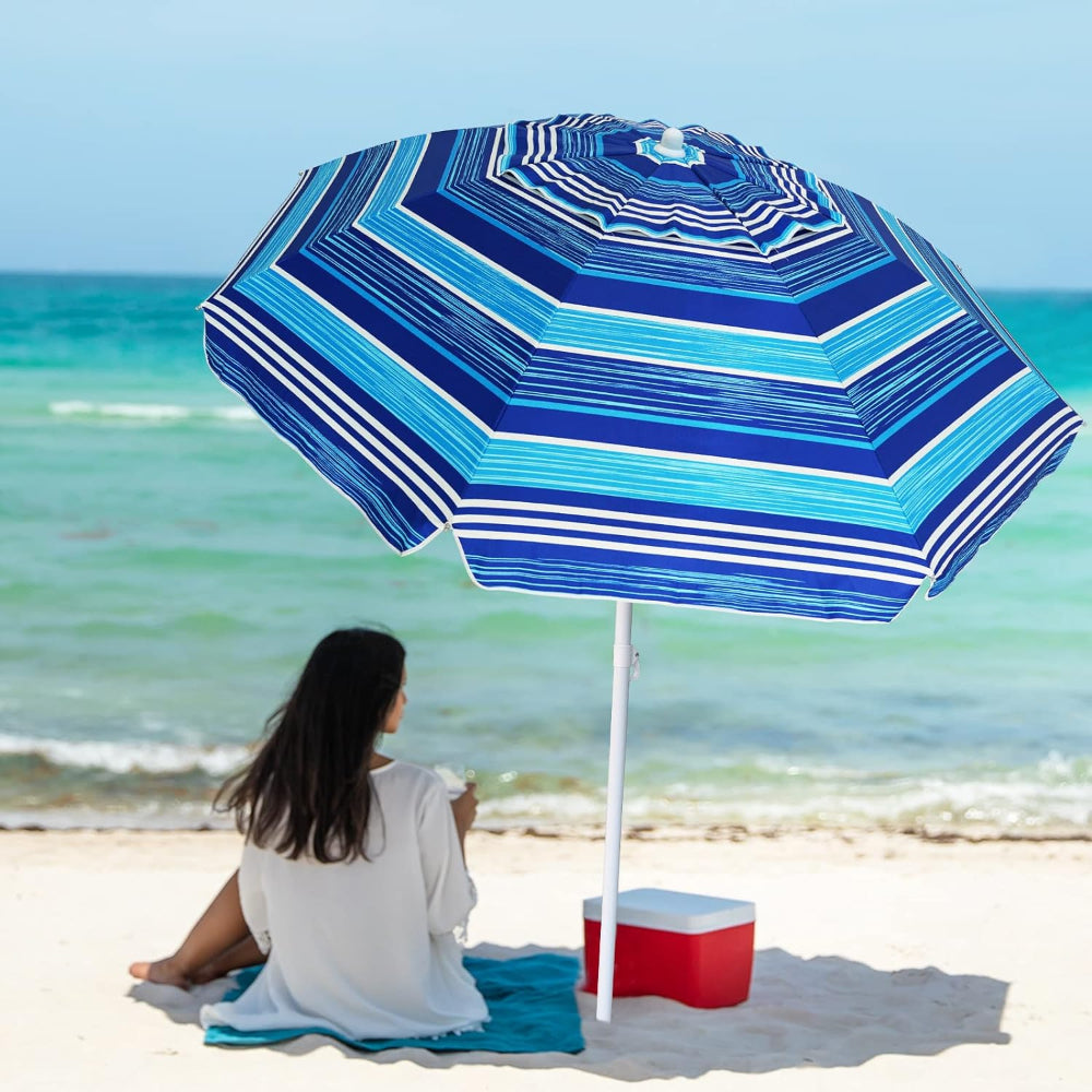 A woman relaxes on the beach, seated under a blue stripes AMMSUN lightweight beach umbrella heavy duty