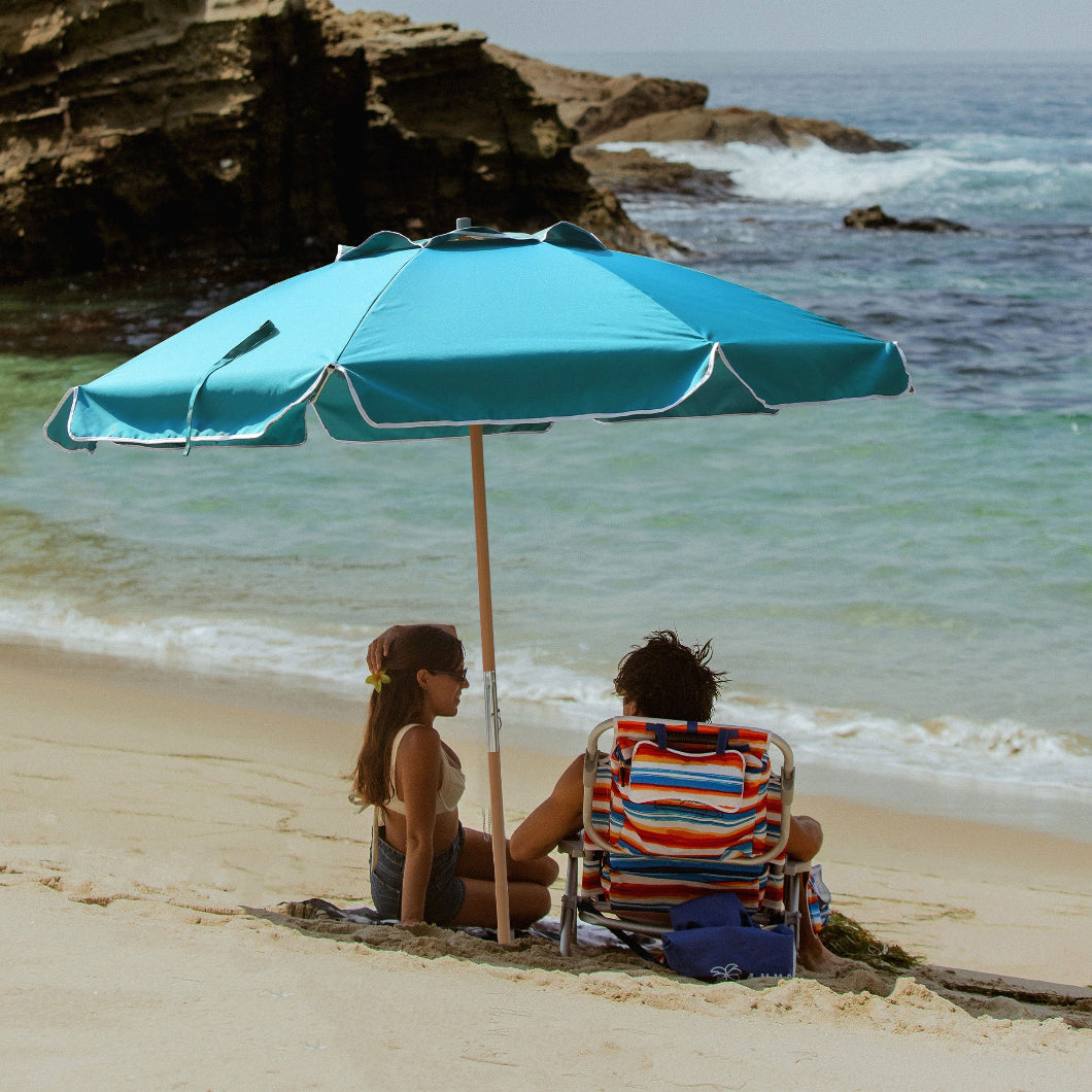 A couple relaxes on a beach, seated under AMMSUN 7.5ft Commercial Grade Teal beach umbrellas clearance