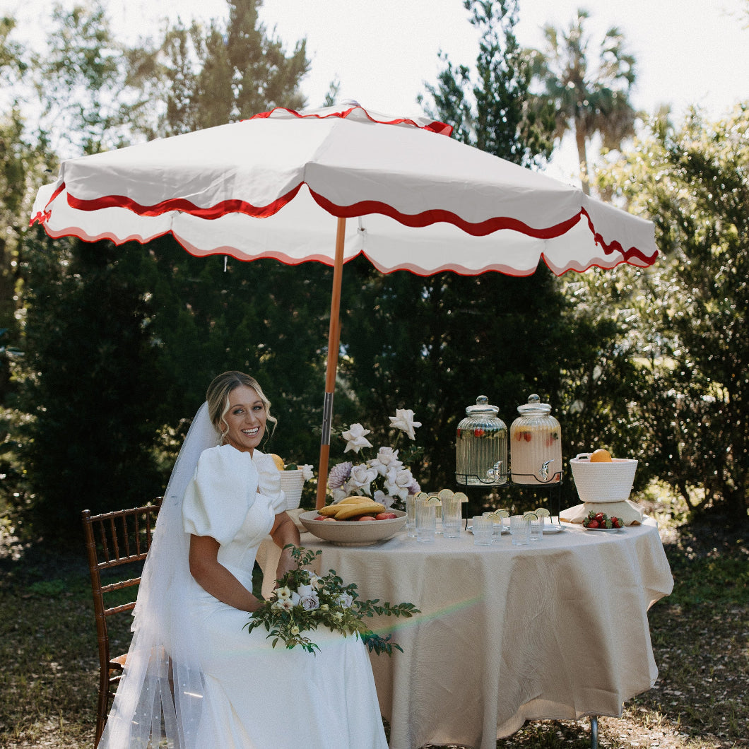 A woman seated at a table, sheltered by AMMSUN 7.8ft red flaps, white boho umbrella for outdoor umbrellas for patio