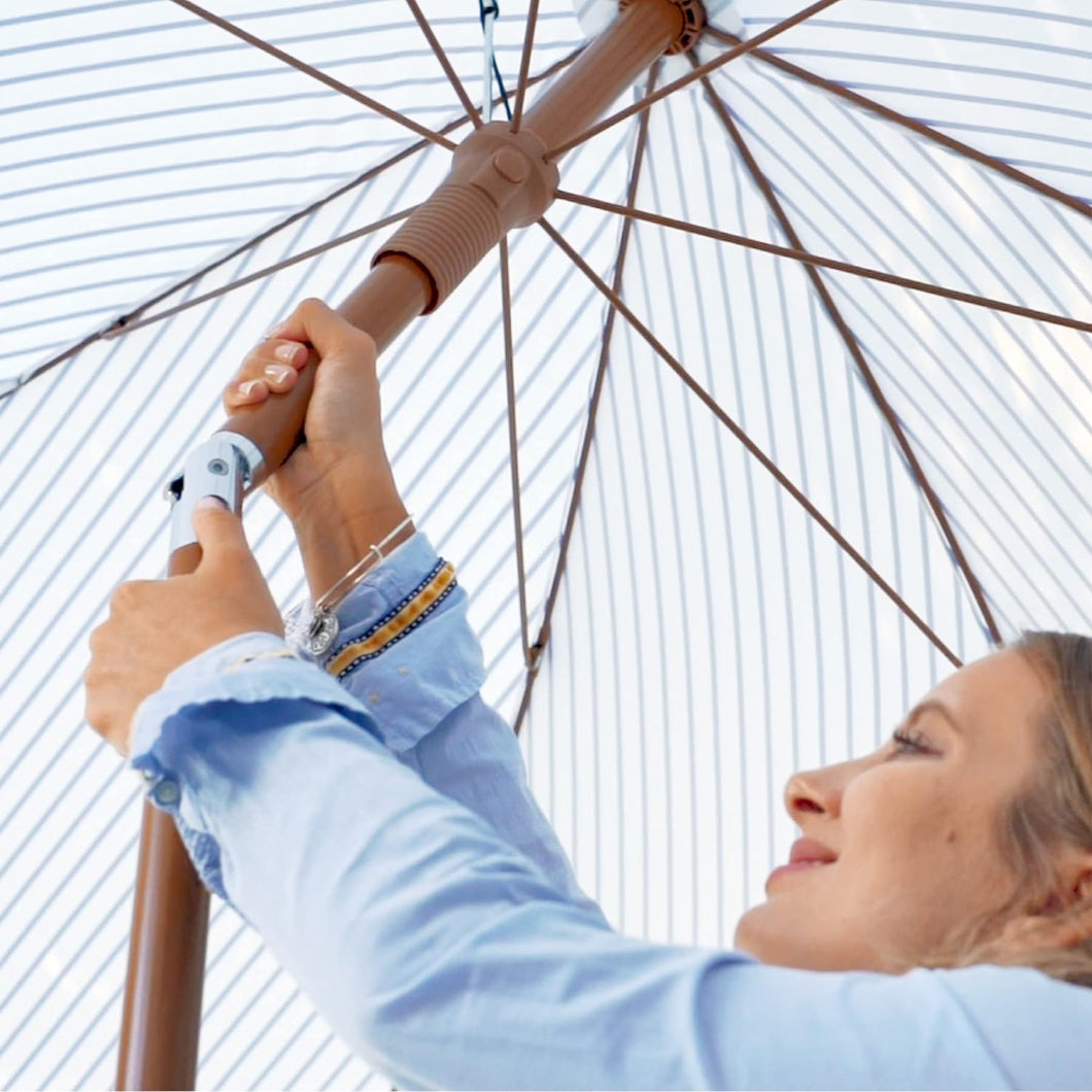 A woman is using the push tilt button on the pole to get AMMSUN 7ft blue stripes fringe umbrellas for patio tables