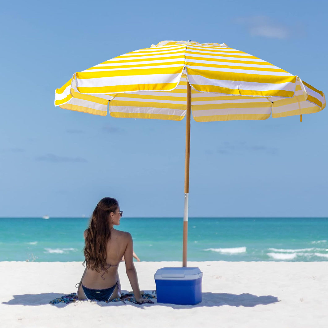 A woman sitting under Ammsun 7.5ft yellow stripes commercial grade portable beach umbrella on beach