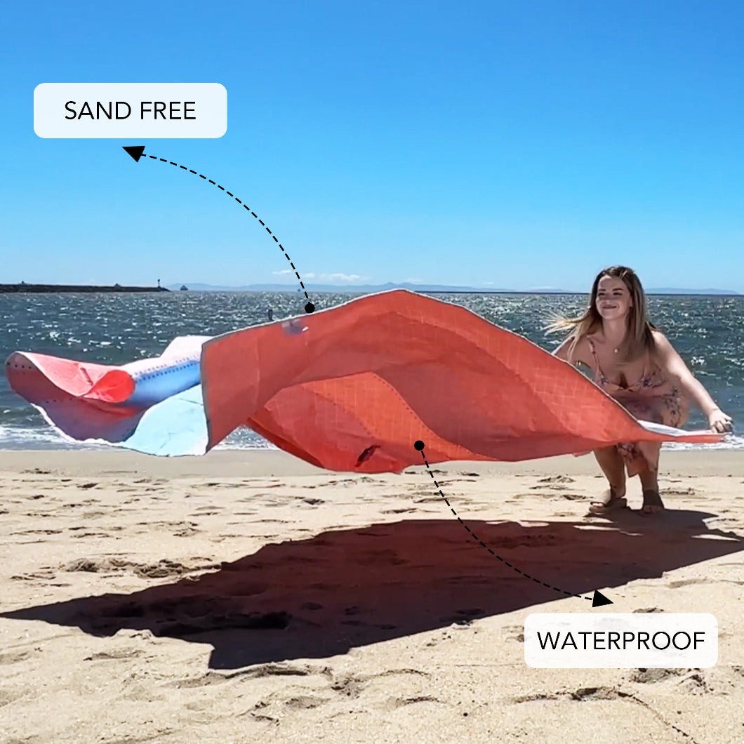 A woman is unfurling an AMMSUN Palette Verse beach compact travel blanket, made of sand free and waterproof fabric