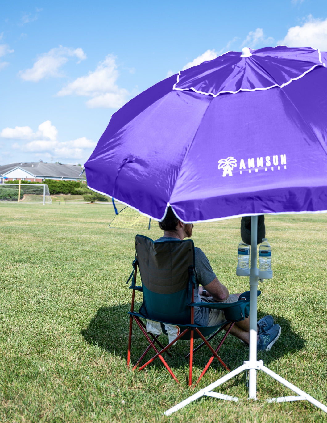 A man sits under AMMSUN 6.5ft purple portable umbrella with stand, putting two bottles of water in the cup holder