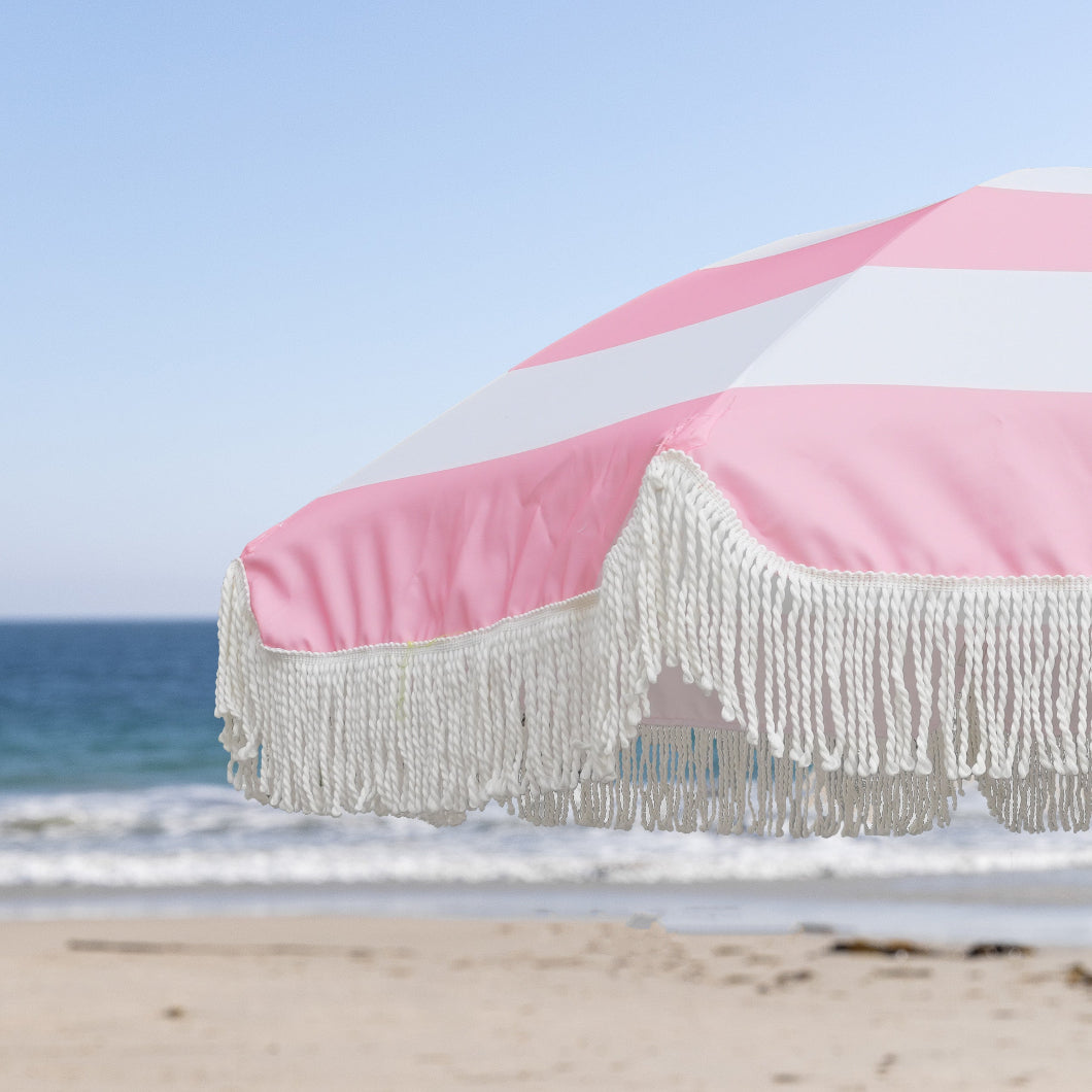 AMMSUN 7ft pink and white striped beach umbrella with white fringe stands on the beach, providing shade for sun