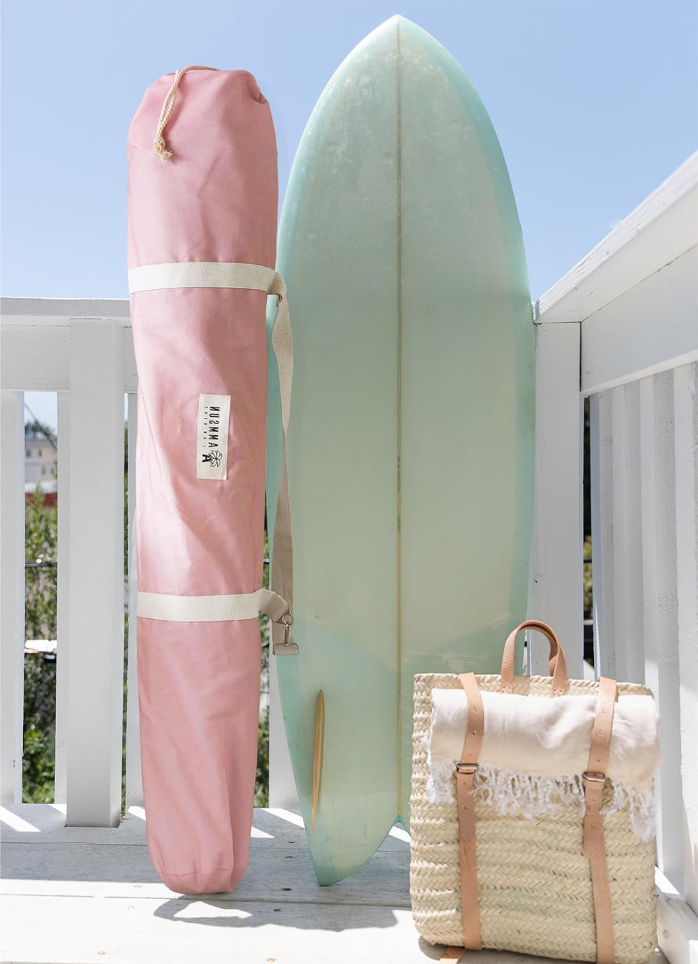 A pink surfboard rests on a deck beside a bag for AMMSUN 6'×6' gentle pink bobo beach cabana cooling tent with fringe