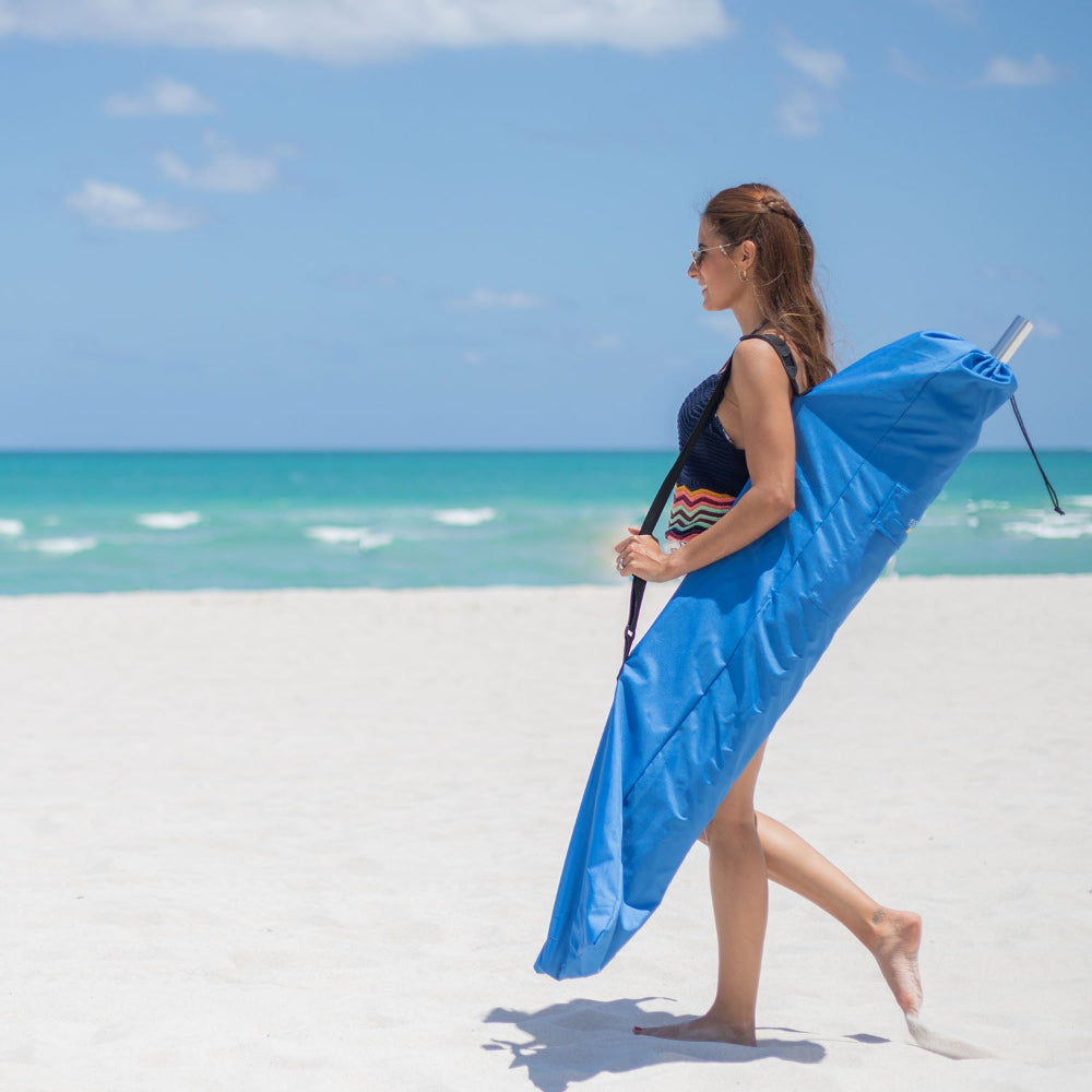 A woman carries a bag for AMMSUN 7.5ft commercial grade blue white travel beach umbrella while walking on beach