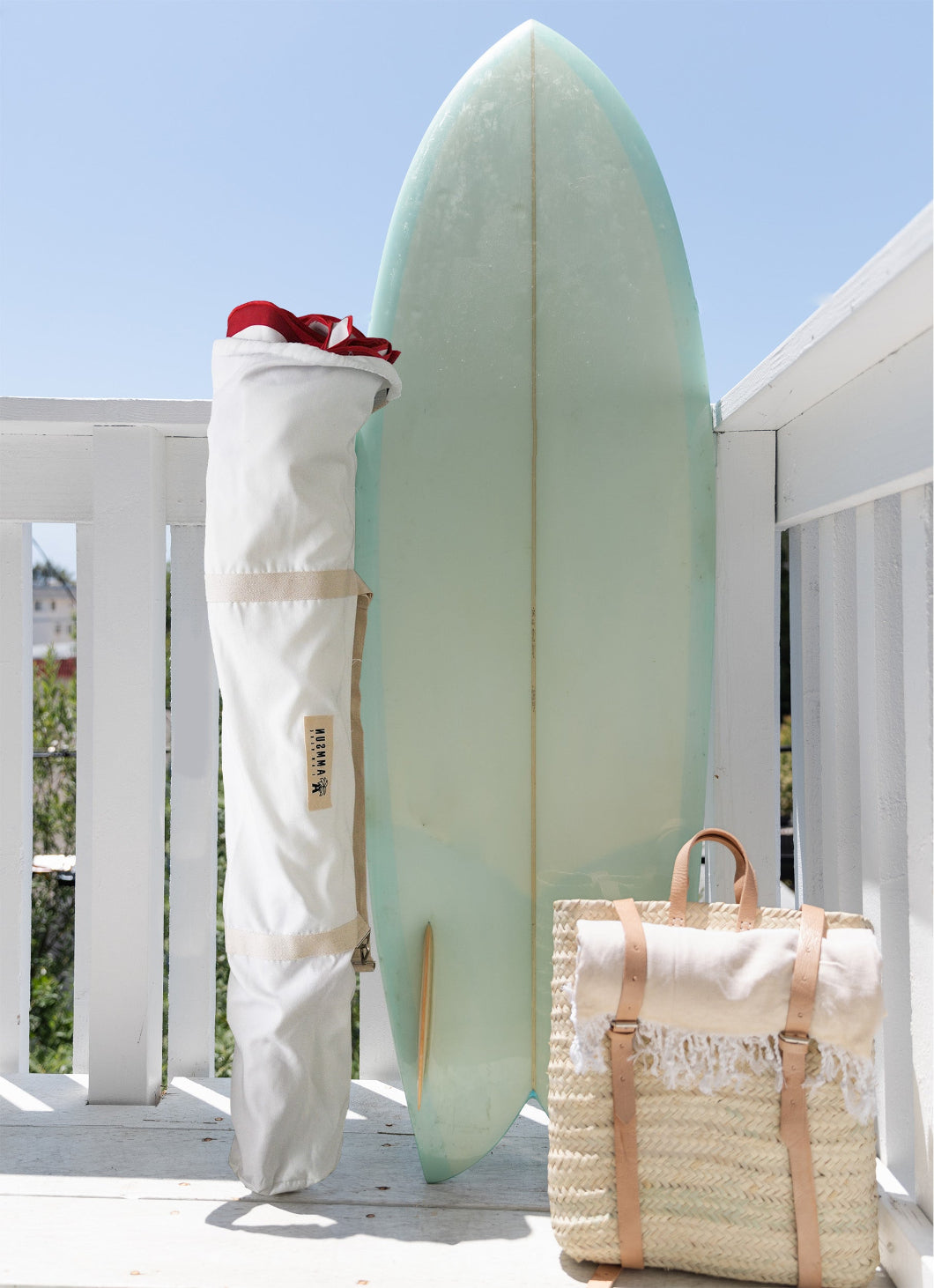 A surfboard rests beside a bag for AMMSUN 7.8ft red flaps, white boho umbrella outdoor patio on a deck