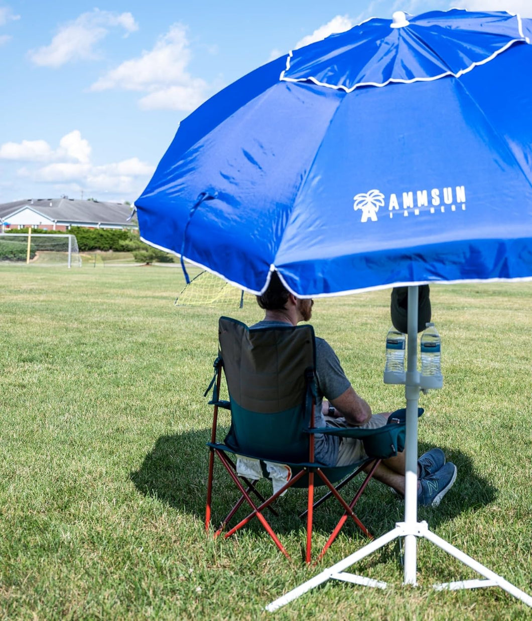 A man seated under an AMMSUN 6.5ft blue umbrella outdoor patio umbrella with base included on a grassy field