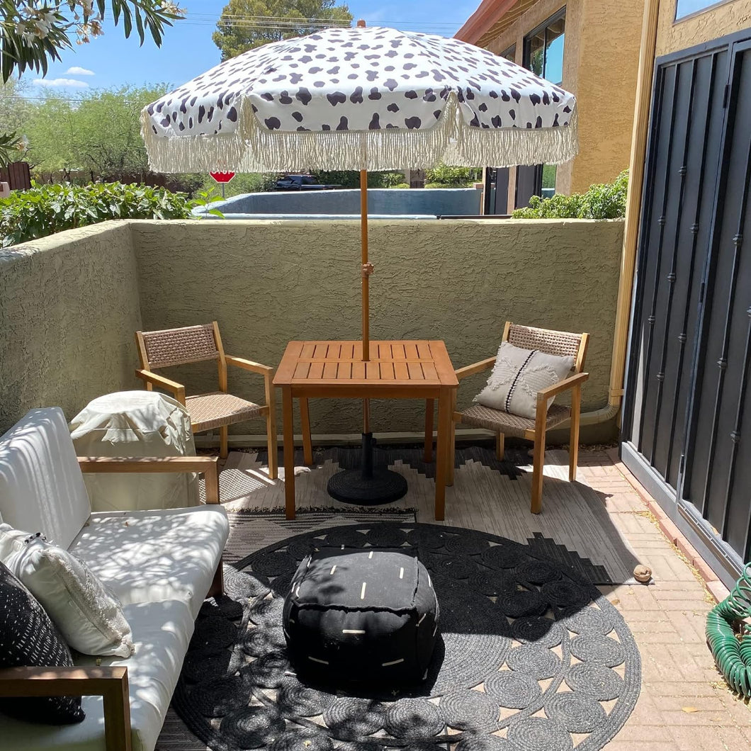 A patio equipped with a table and chairs, shaded by AMMSUN 7ft Cow Polka Dots fringe yard umbrella