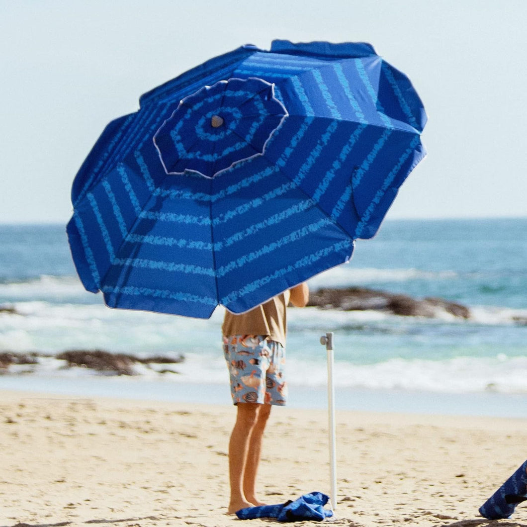 A man is putting AMMSUN 7ft blue pattern patio umbrellas into white lower pole with sand anchor on beach