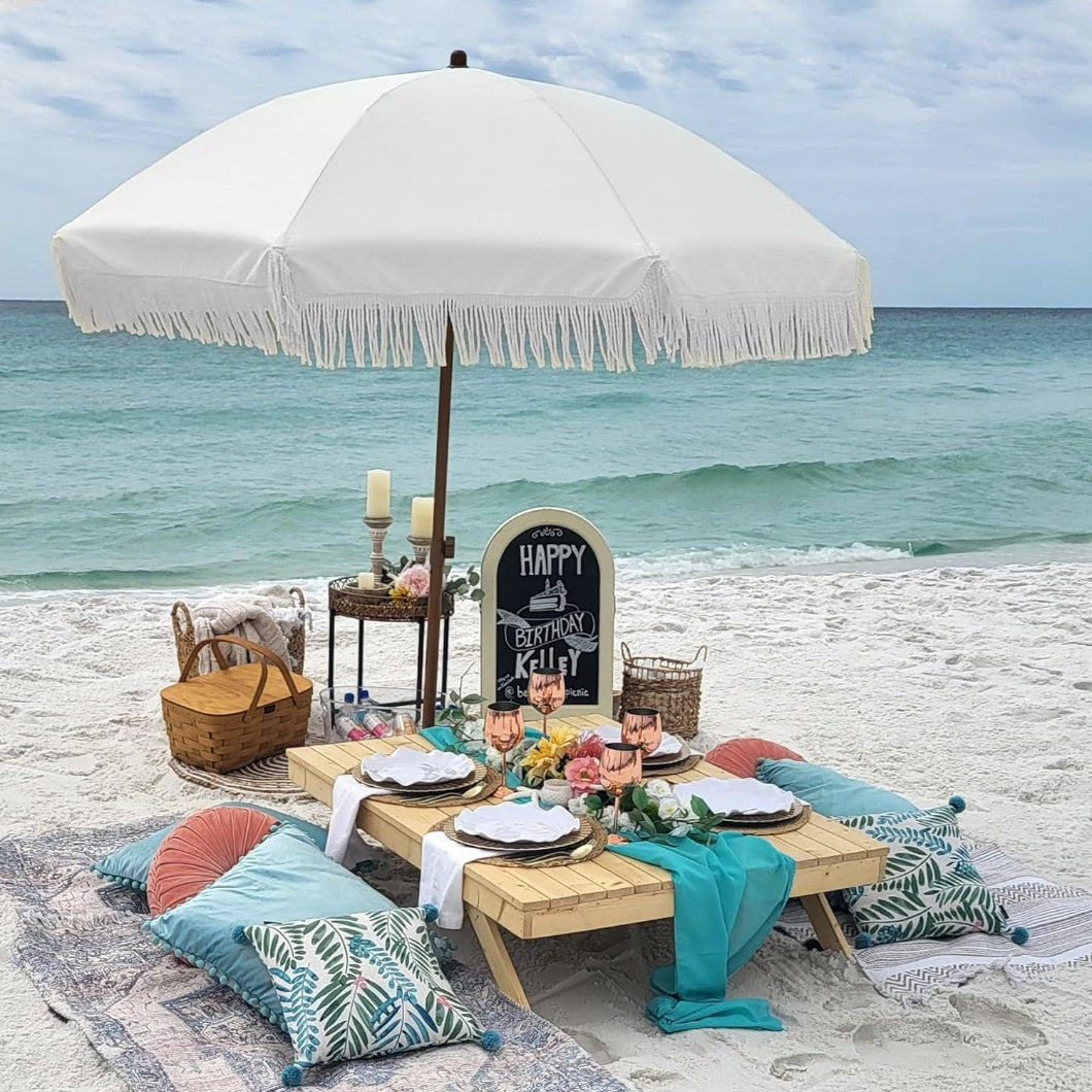 A beach picnic table shaded by AMMSUN 7ft elegant cream umbrella for table with fringe sunbrella