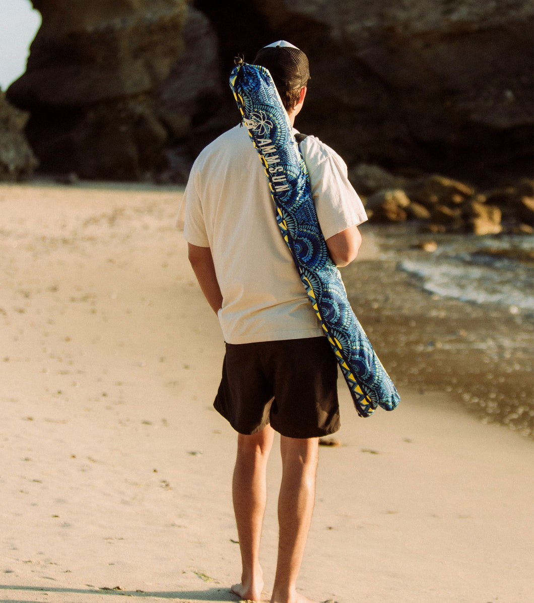 A man is carrying the bag on his shoulder for AMMSUN Revival Blues 7ft beach shade umbrella with sand anchor