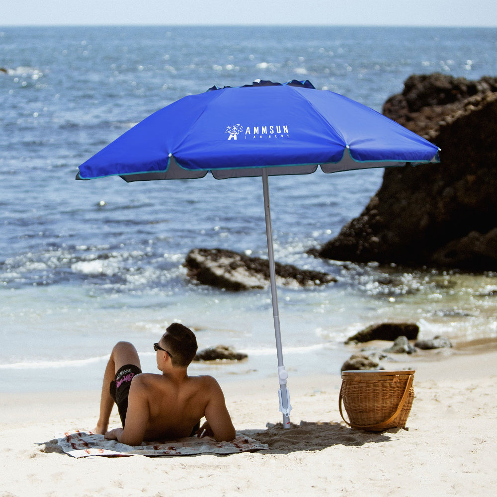 A man sits under AMMSUN 6.5ft navy blue twice folded portable beach umbrellas for sand with sand anchor