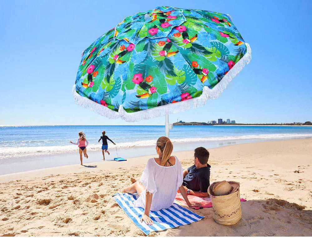 Two individuals relax on the beach beneath a colorful AMMSUN 6.5ft tropical fringe travel beach umbrella