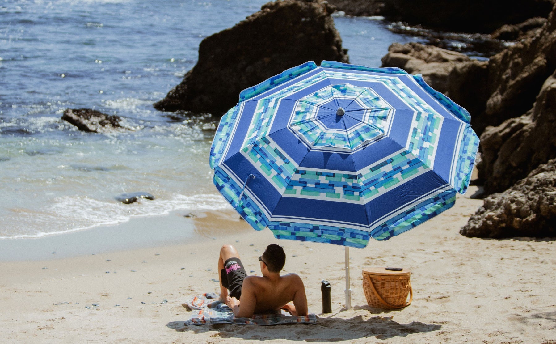 A man lying under AMMSUN 7ft ice blue stripes heavy duty umbrellas for rain with sand anchor