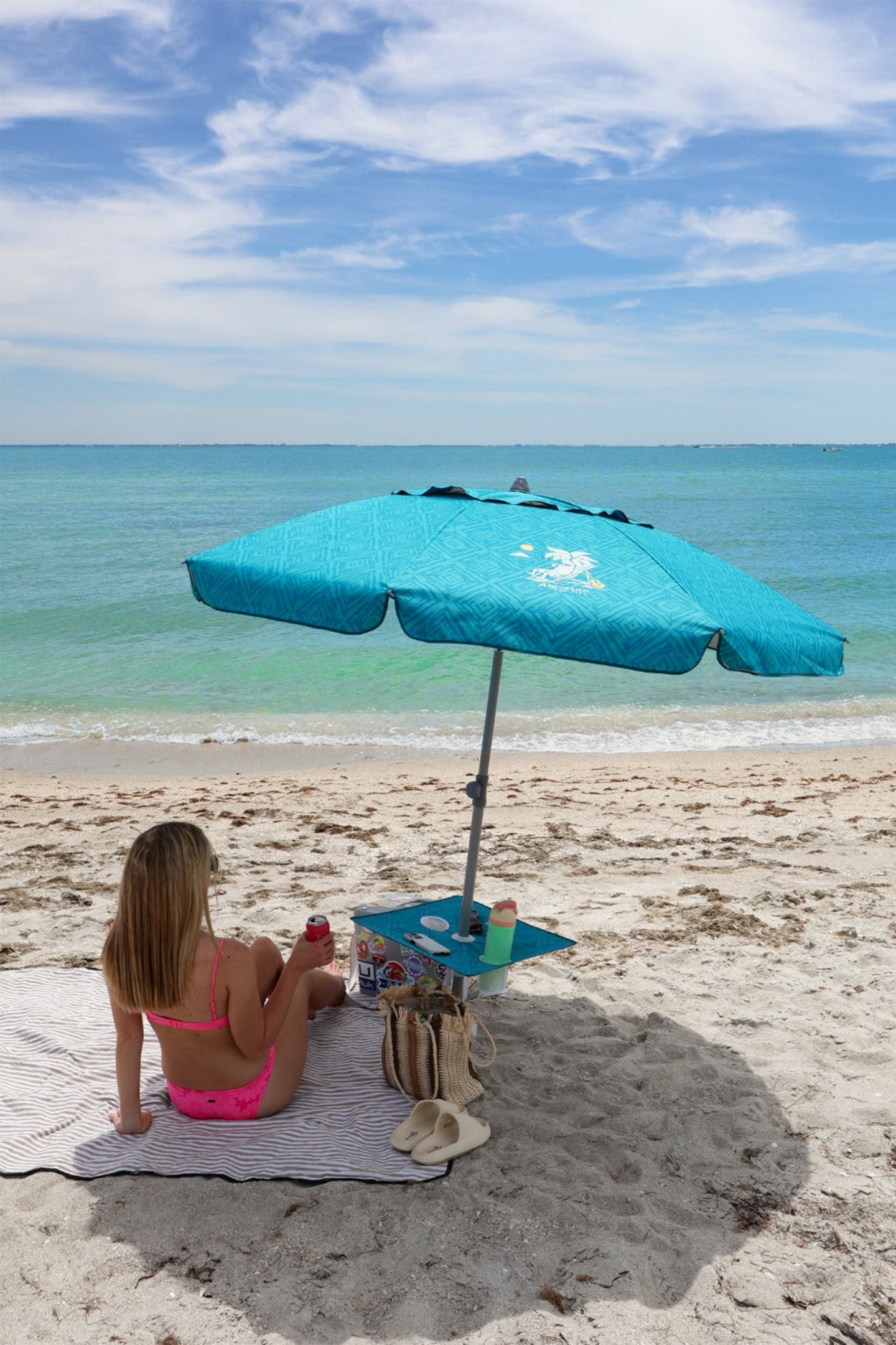 A woman sitting under AMMSUN 7ft sky blue beach umbrella with sand anchor and table tray，Enjoy the sun on the beach