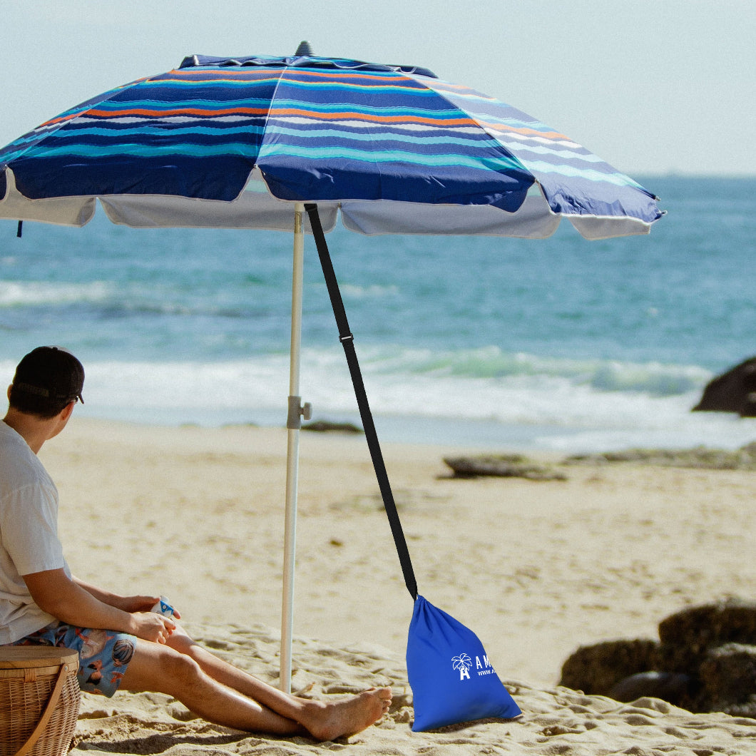 A man is sitting under a beach umbrella secured by AMMSUN tent sand bags weights on sand for sand bags